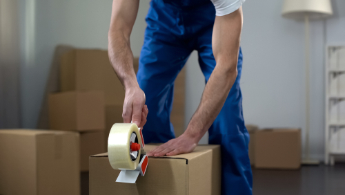 Man packing and taping a cardboard moving box.